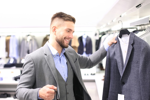 Jeune homme élégant choisissant un nouveau costume dans un centre commercial ou un magasin de vêtements.