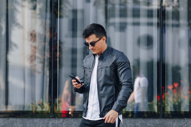 Jeune homme élégant dans des verres en veste de cuir noir avec téléphone