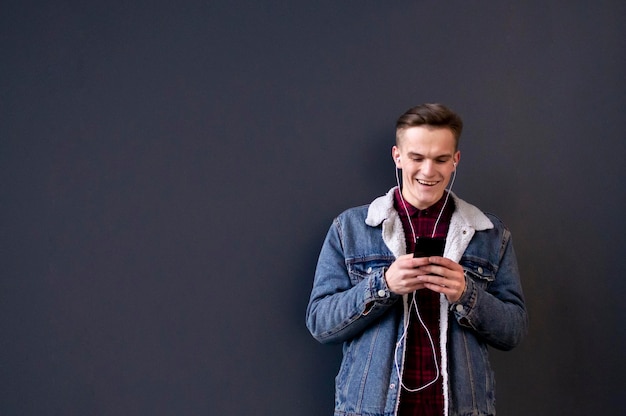 Jeune homme élégant dans une veste en jean et une chemise écoute de la musique sur des écouteurs