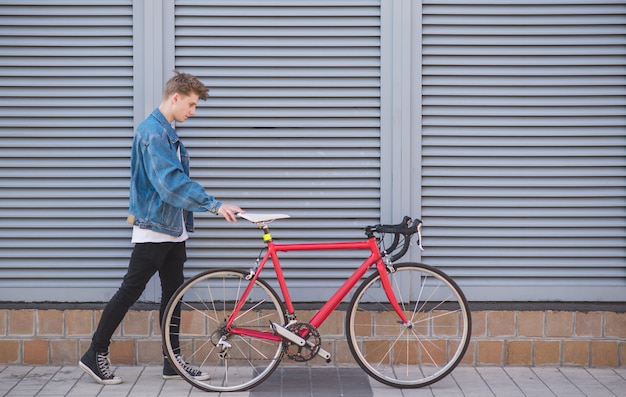 Jeune homme élégant dans une veste en jean et un vélo sur une surface grise