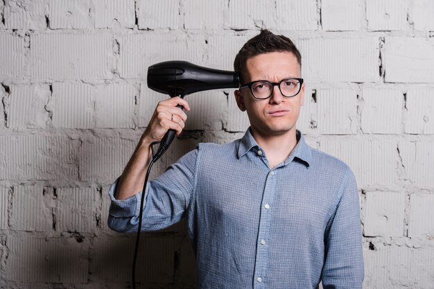 Jeune homme élégant fou avec coiffure et expressions drôles sur le mur de briques grises