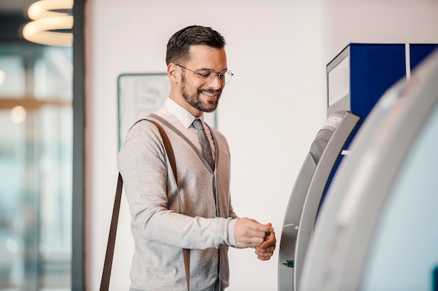 Un jeune homme élégant et heureux utilise un guichet automatique dans un centre commercial