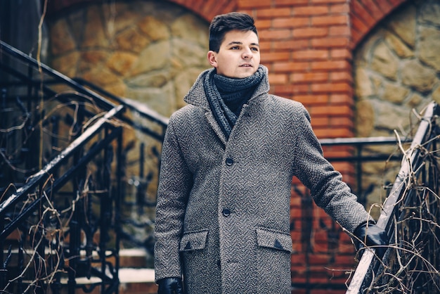 Jeune homme élégant en manteau gris chaud et des gants en cuir en descendant les escaliers