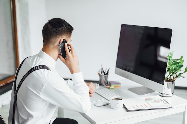 Jeune homme élégant avec un ordinateur portable au bureau, isolé sur blanc.