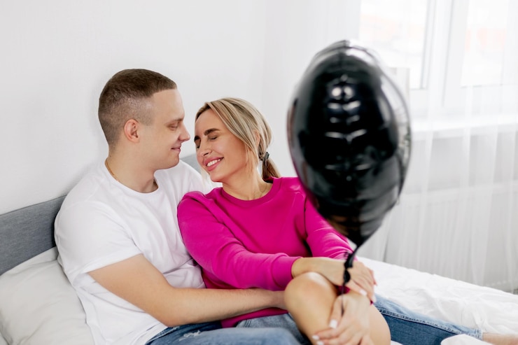 Photo un jeune homme embrasse une fille assise sur un lit avec un ballon en forme de cœur pendant la célébration de la saint-valentin.