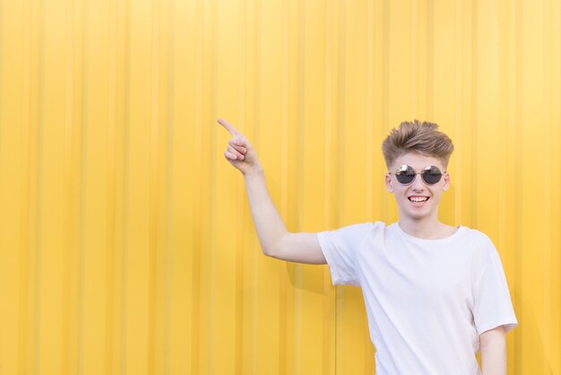 Un jeune homme émotif se tient sur un mur orange et montre ses mains de côté à l'endroit pour le texte. Copyspace