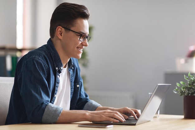 Jeune homme employé de l'entreprise travaillant avec un ordinateur portable dans la vue latérale du bureau