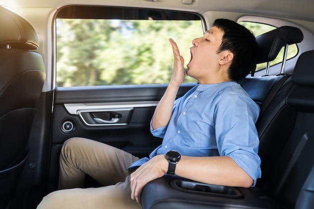 Jeune homme endormi bâillant alors qu'il était assis sur le siège arrière de la voiture