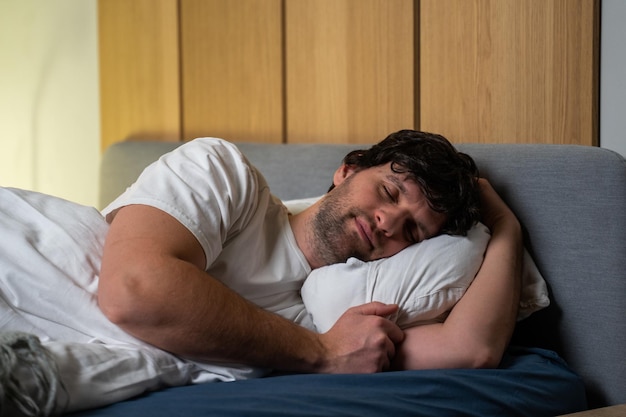 Jeune homme endormi se reposant paisiblement dans un lit confortable allongé les yeux fermés Le concept de temps de repos et de sieste