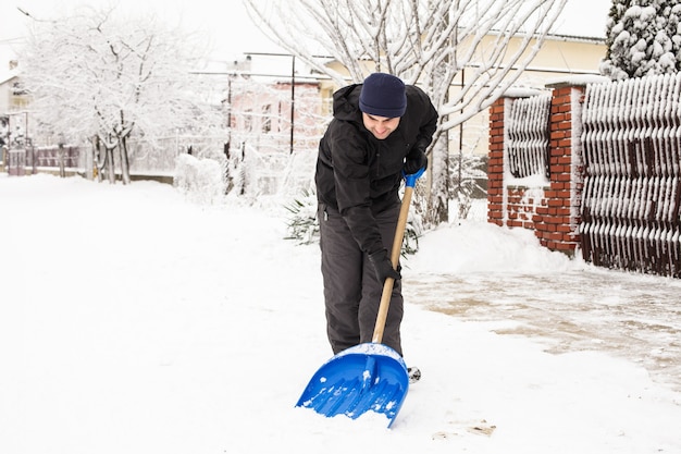 Le jeune homme enlève la neige près de la maison de banlieue