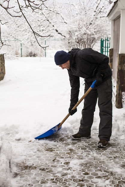 Le jeune homme enlève la neige près de la maison de banlieue