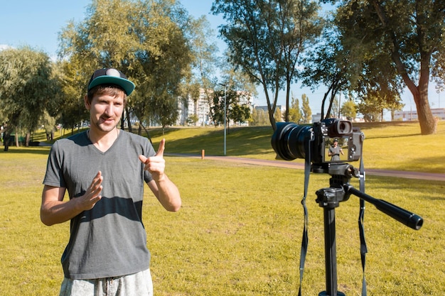 Un jeune homme enregistre un blog vidéo sur la caméra dans le parc