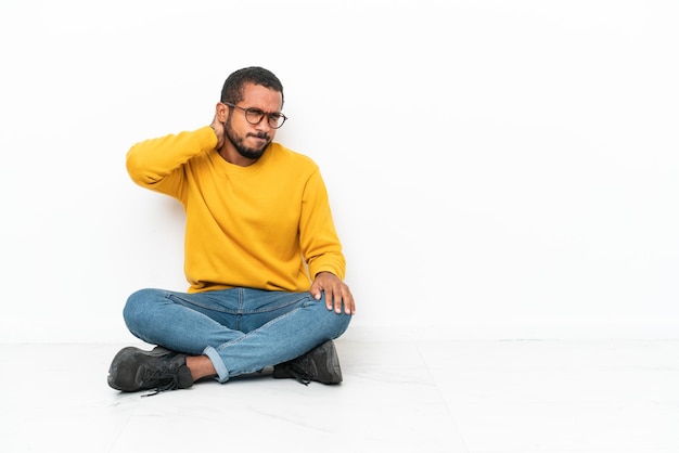 Jeune homme équatorien assis sur le sol isolé sur mur blanc avec mal de cou