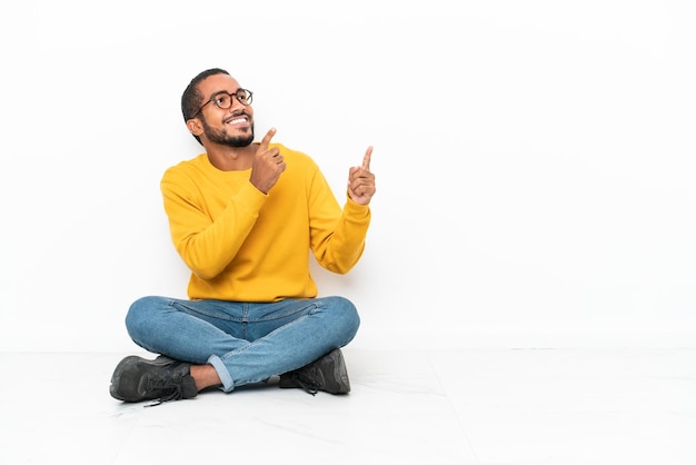 Jeune homme équatorien assis sur le sol isolé sur mur blanc pointant avec l'index une excellente idée