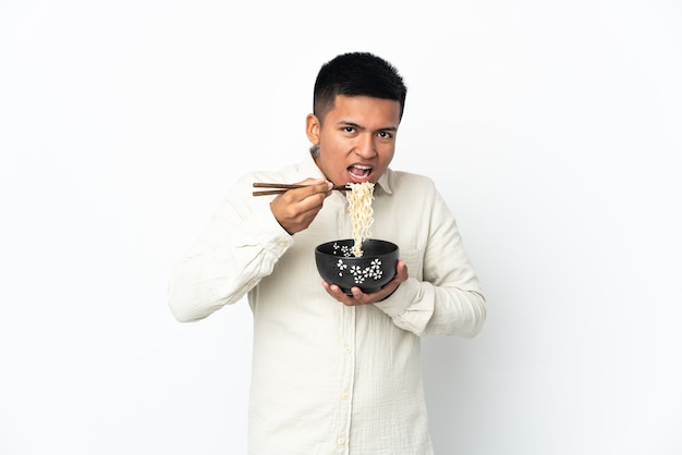 Jeune homme équatorien isolé sur fond blanc tenant un bol de nouilles avec des baguettes et le manger