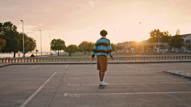 Jeune homme équilibrant la planche à roulettes le soir vue arrière mec actif équitation longboard