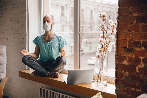 Jeune homme équilibré faisant du yoga à la maison tout en étant en quarantaine et travaillant en ligne en indépendant