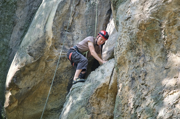 Jeune homme escaladant le mur escarpé de la montagne rocheuse. Grimpeur mâle surmonte la route difficile. S'engager dans le concept de sport extrême.