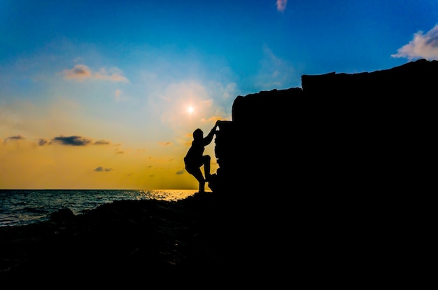 Jeune homme, escalade, falaise verticale, à, coucher soleil, sur, océan