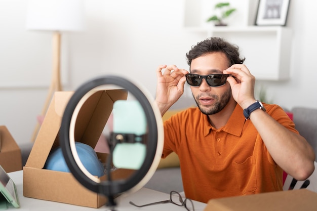 Jeune homme essayant des lunettes de soleil tout en enregistrant une vidéo pour les médias sociaux