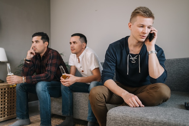 Jeune homme essayant de parler au téléphone derrière des amis regardent la télévision