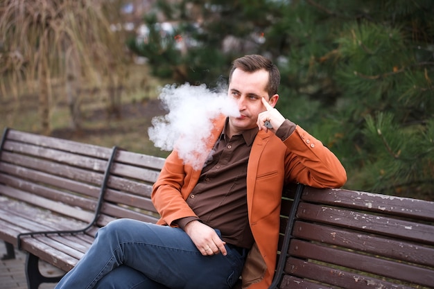 Un jeune homme est assis sur un banc et fume une cigarette électronique