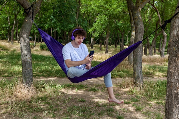 Photo un jeune homme est assis dans un hamac violet à l'écoute de musique sur des écouteurs en profitant de la nature