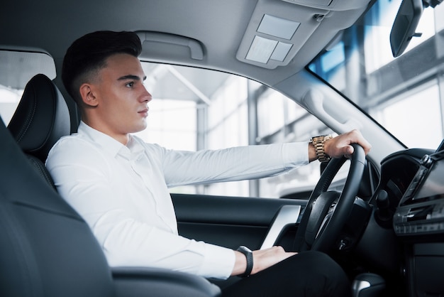 Un jeune homme est assis dans une voiture nouvellement achetée au volant, un achat réussi.