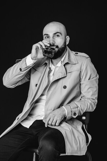 Un jeune homme est assis sur un mur noir et boit une boisson alcoolisée. Noir et blanc.