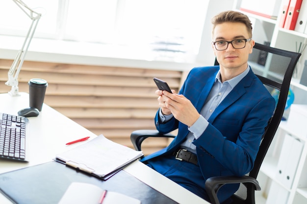 Un jeune homme est assis avec un téléphone dans ses mains à une table du bureau.