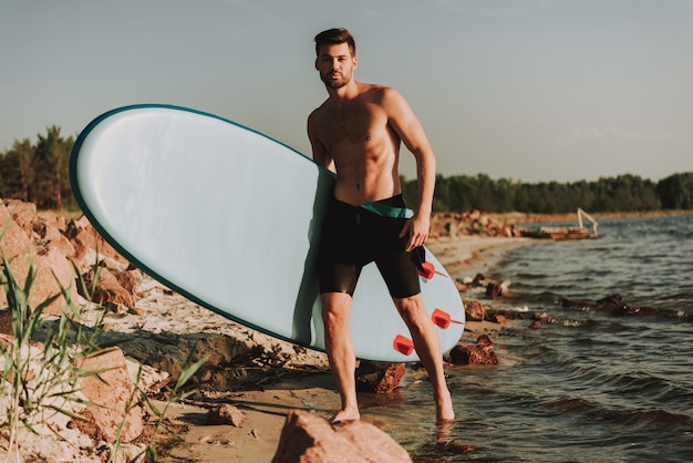 Jeune homme est debout sur la plage avec surf