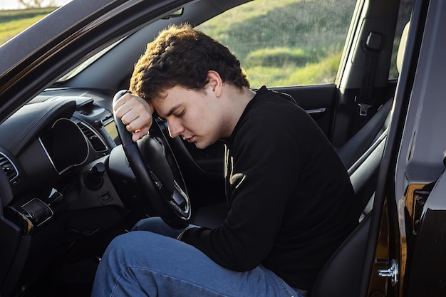 un jeune homme est fatigué sur la route et dort sur le volant d'une voiture