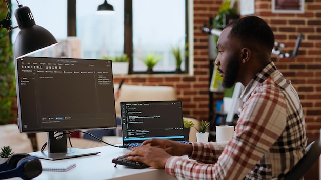 Un jeune homme est vu en train de programmer un code logiciel sur son ordinateur portable dans un bureau à domicile élégant.