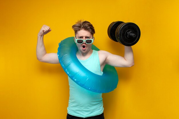 Jeune homme en été en vacances avec un anneau de natation gonflable tient un gros haltère lourd