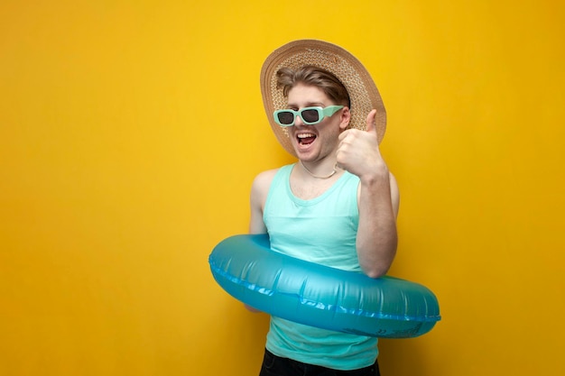 Jeune homme en été en vacances avec un cercle de natation gonflable et des lunettes de soleil montre comme