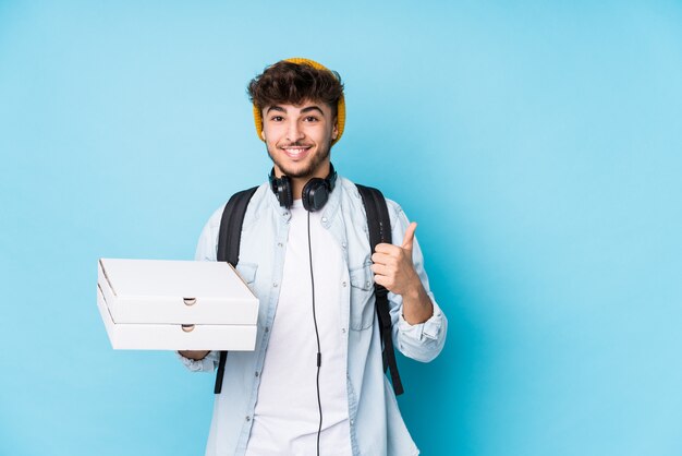 Jeune homme étudiant arabe tenant des pizzas souriant et levant le pouce vers le haut