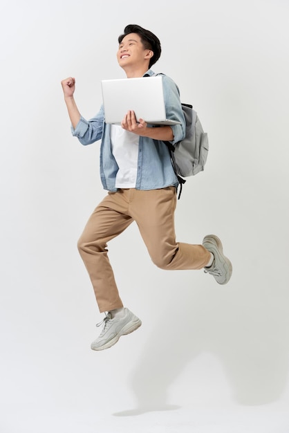 Jeune homme étudiant asiatique sautant dans l'air à l'aide d'un ordinateur portable avec sac à dos isolé sur fond blanc