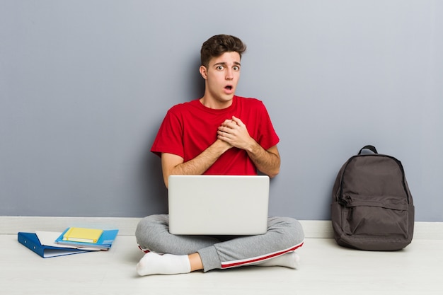 Jeune homme étudiant assis sur le sol de sa maison tenant un ordinateur portable