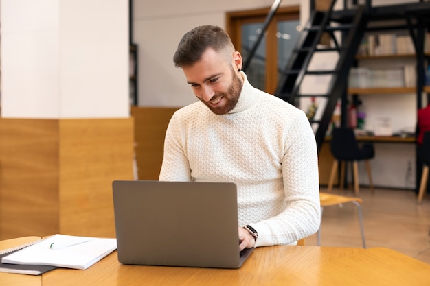 Photo jeune homme étudiant dans une bibliothèque à l'aide de son ordinateur portable