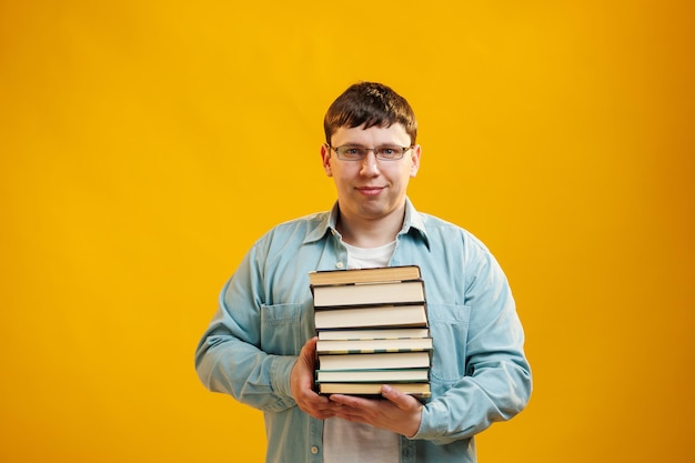 Jeune homme étudiant dans des verres tient une pile de livres universitaires de la bibliothèque du collège sur fond jaune Un gars heureux sourit qu'il est heureux d'obtenir un diplôme à l'étranger concept Espace de copie