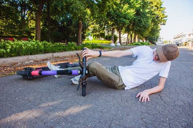 Photo un jeune homme a eu un accident sur un scooter électronique, s'allonge sur l'asphalte et hurle de douleur