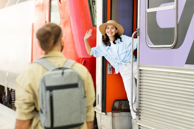 Un jeune homme européen rencontre une femme heureuse agitant la main au train à la gare en plein air