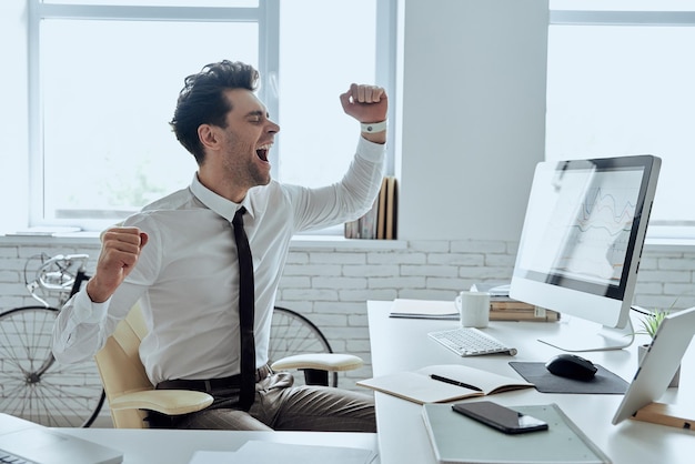 Un jeune homme excité en chemise et cravate fait des gestes alors qu'il est assis à son bureau.