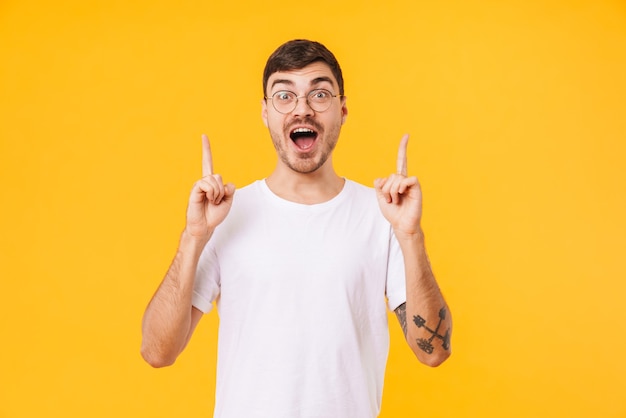 jeune homme excité à lunettes pointant les doigts vers le haut isolé sur un mur jaune