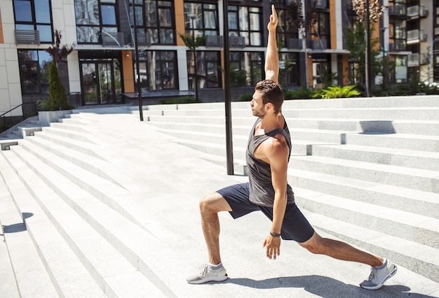 Photo jeune homme exerçant à l'extérieur. guy debout en position semi-accroupie ou pose de yoga tenant les mains de haut en bas en même temps. guy s'occupe du corps et de la silhouette. s'entraîner seul à l'extérieur.