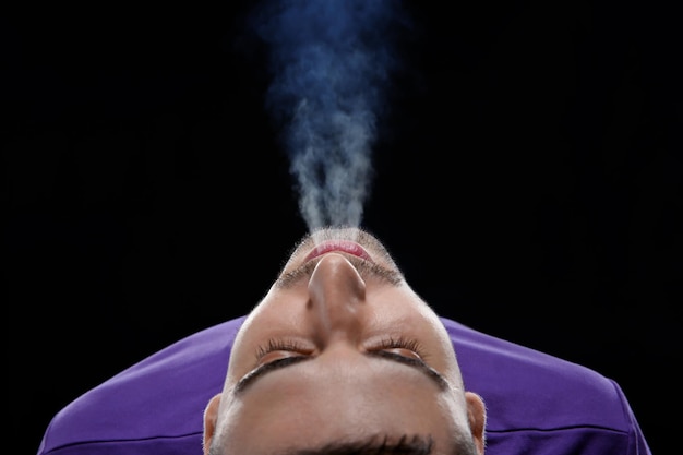 Jeune homme exhalant de la fumée sur fond noir