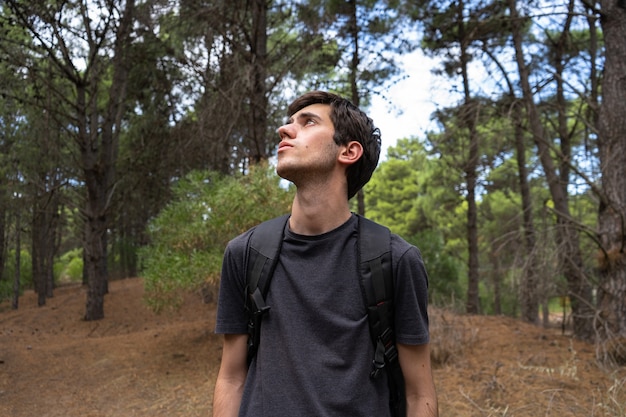 Jeune homme explorant une forêt et regardant les arbres