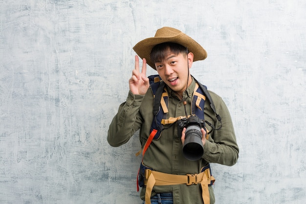 Jeune homme explorateur chinois tenant un appareil photo amusant et heureux de faire un geste de victoire