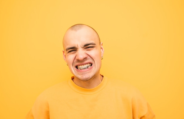 Jeune homme expressif avec un grillz sur ses dents est en colère contre un jaune