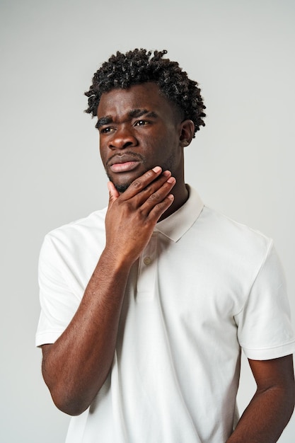 Un jeune homme avec une expression pensive touchant son menton sur un fond gris